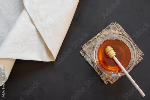 Organic fresh liquid honey in glass bowl with dipper on rustic background, healthy food photo