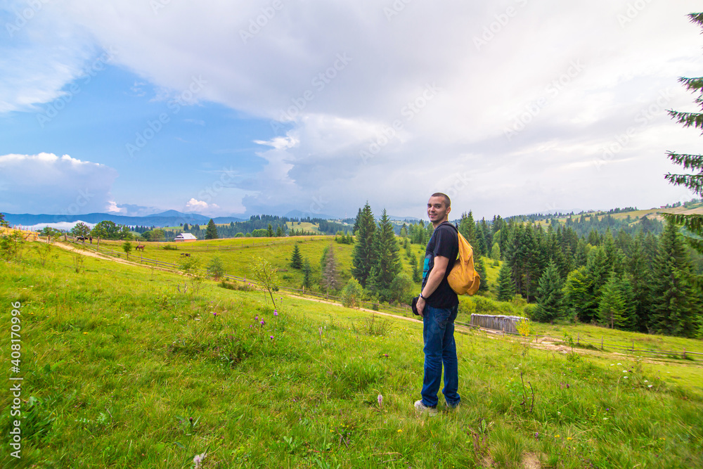 A guy travels with a yellow backpack through picturesque places with beautiful mountain landscapes
