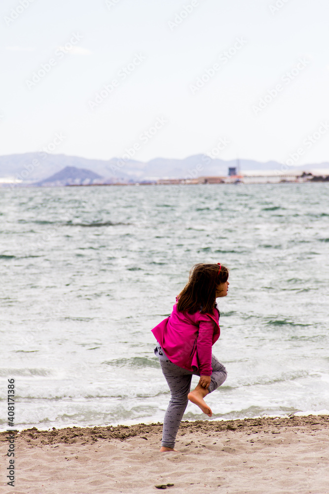 girl in winter clothes barefoot on the beach, with pink jacket