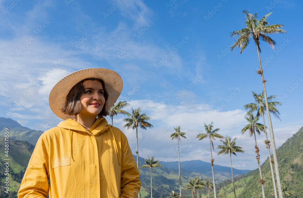 A traveling woman with a hat on poses in front of a beautiful landscape of wax palms. traveling woman. female hiker
