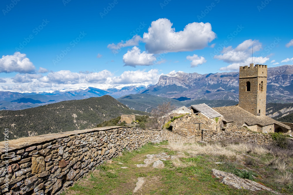 medieval walled village in ruins with a crenellated tower and snow-capped mountains in the background, walled enclosure of Muro de la Roda, La Fueva, Sobrarbe, Huesca Pyrenees, Spain
