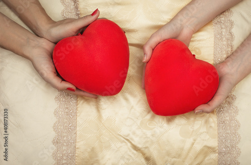 LGBT concept. Womens hands holding red hearts in the bed. Hands of couple of homosexual women on yellow set sail champagne color pillow. Same sex love. Lesbi relationships. photo