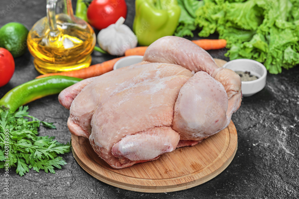 Raw whole chicken with lettuce, peppers, spices and tomatoes on wooden plate Raw whole chicken with lettuce, peppers, spices and tomatoes on wooden plate