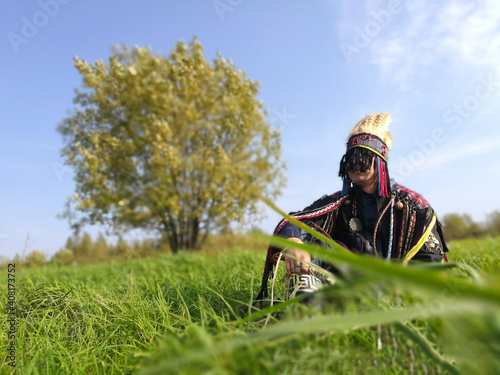 young shaman sits on a lawn near a tree.