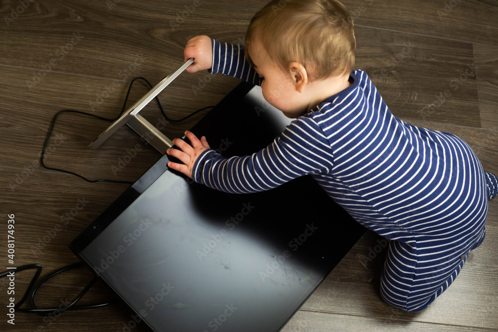 Naughty caucasian baby boy in blue pyjamas is playing with a tv, monitor destroyed by himself. Damage and devastation of electronic items at home caused by a curious toddler.
