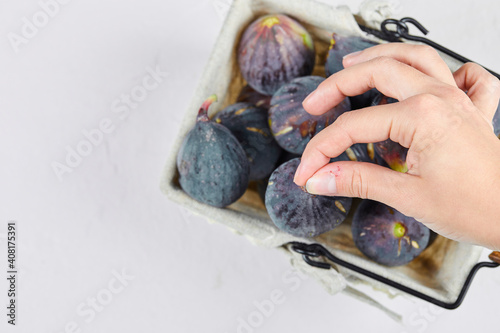 Hand holding a fig from the basket on a white background