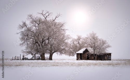 Old farmhouse in winter on the rural eastern plains of Colorado. The trees are frosted with ice and snow is on the ground. 