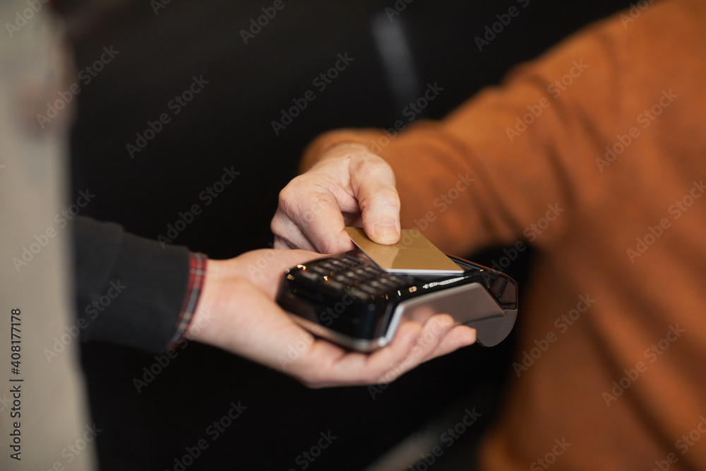 Close up of unrecognizable mature man paying with credit card, focus on hands holding card over terminal, copy space Close up of unrecognizable mature man paying with credit card, focus on hands holding card over terminal, copy space
