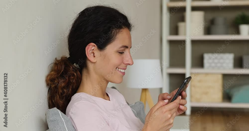 Head shot close up side view smiling millennial beautiful caucasian woman enjoying using dating application on smartphone, playing online mobile game or communicating distantly with friends at home. Head shot close up side view smiling millennial beautiful caucasian woman enjoying using dating application on smartphone, playing online mobile game or communicating distantly with friends at home.