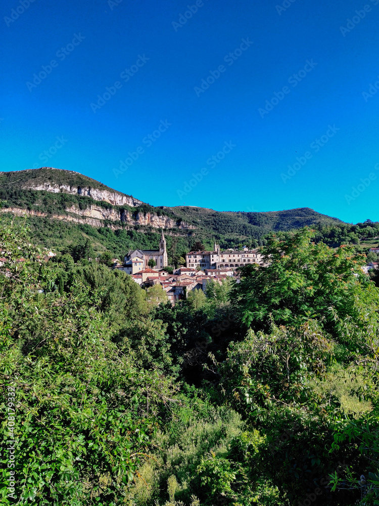 A panoramic view of a small old French village surrounded by nature during a summer day over a blue cloudy sky. Aveyron, France.