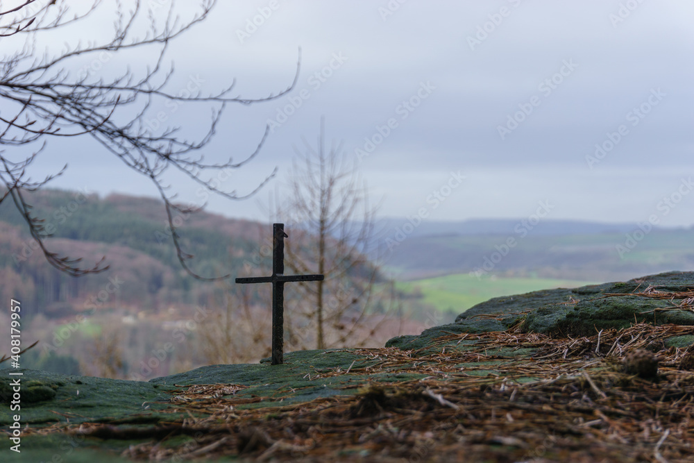 small iron cross on rock formation with blurry landscape in background