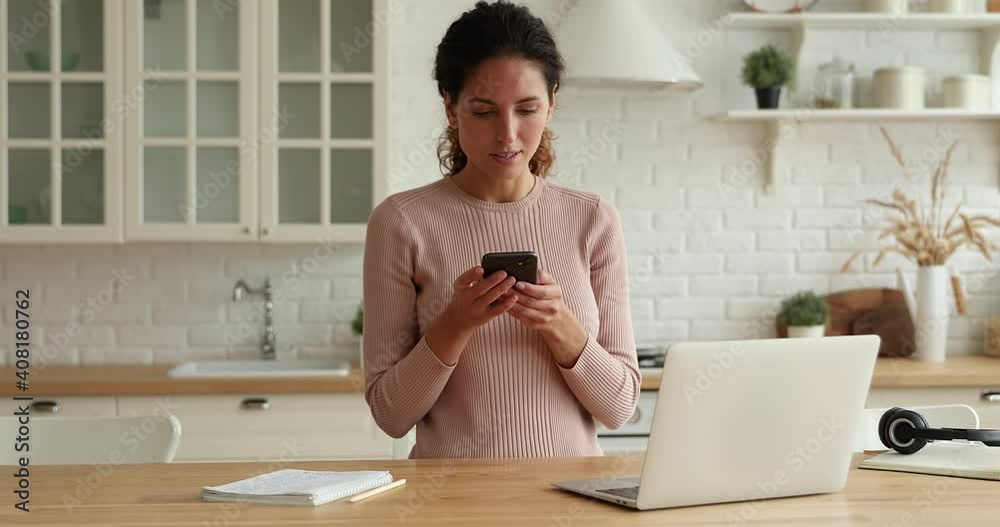 Happy young beautiful woman working on laptop, getting message notification with online lottery win, feeling overjoyed at home, celebrating professional or gambling success, dancing alone in kitchen.