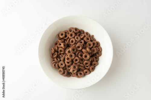 Chocolate cereal rings falling in bowl isolated on white background, top view