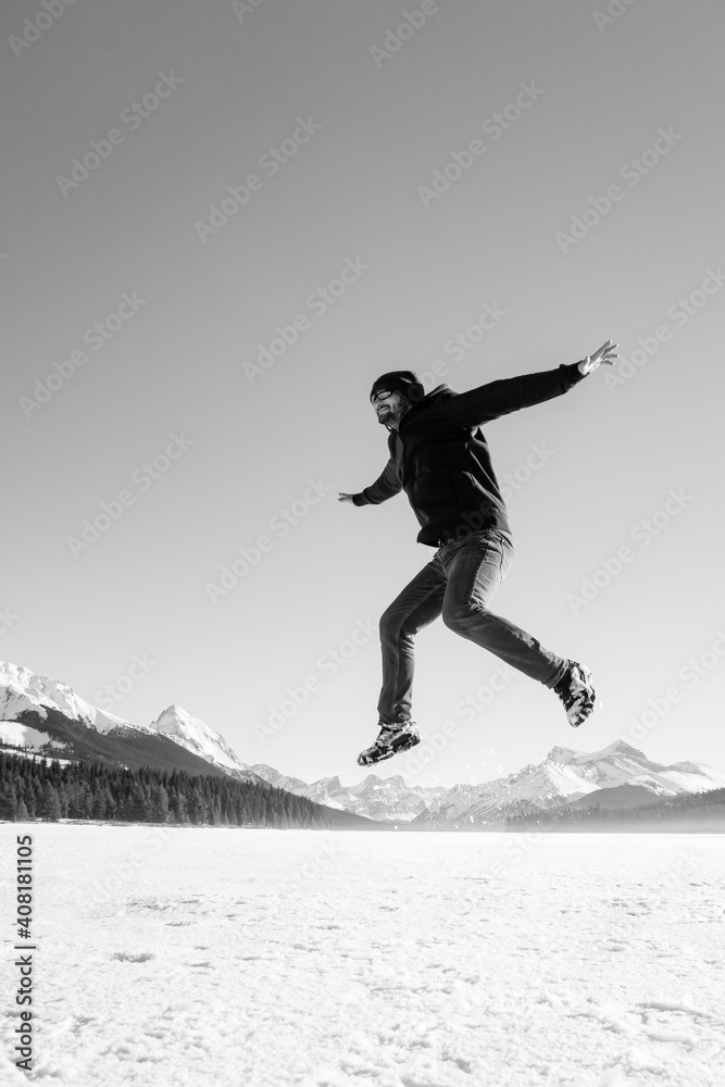 Black and white photography of a young man jumping in the air at Maligne Lake, Canada