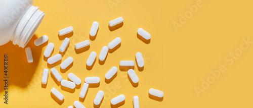 White pills are poured from a jar on a yellow background. Food supplement, multivitamins, medications