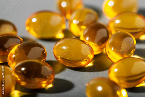 Yellow gelatin capsules on a gray background. Food supplement, vitamin D, omega, vitamin C, multivitamins. Soft focus