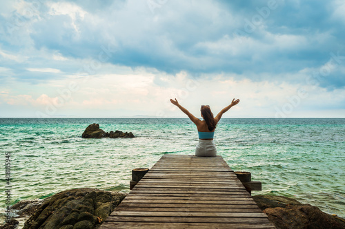 happy woman sitting on a wooden bridge with arm raised in the sea at Koh MunNork Island, Rayong, Thailand