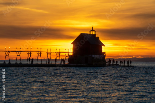 Grand Haven Lighthouse Michigan on Lake Michigan at sunset during the winter with beautiful colors and the structures and people silhouetted. Hot from North Pier.
