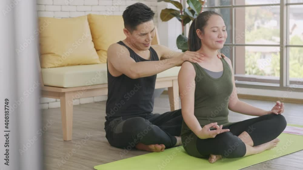 Happy Asian beautiful lifestyle family couple, woman doing YOGA sitting meditating on lotus pose workout at home and the man massage shoulder for relax. sport healthy concept Happy Asian beautiful lifestyle family couple, woman doing YOGA sitting meditating on lotus pose workout at home and the man massage shoulder for relax. sport healthy concept