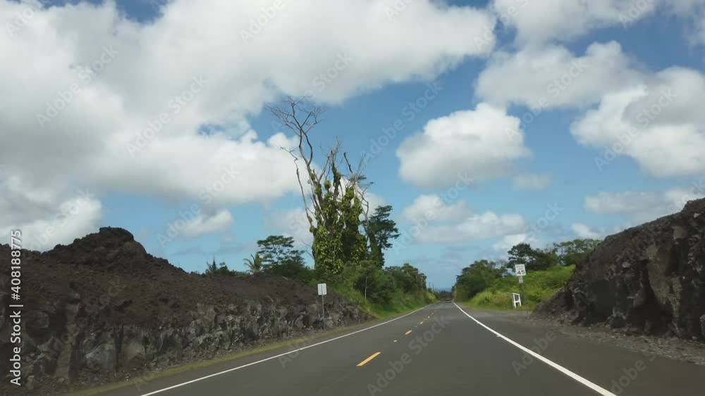 Driving through lava that has been cleared for a new road after a recent eruption on Hawaii with surviving vegetation and homes