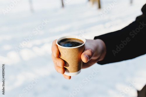 The guy holds a paper cup of coffee in his hand in the snowy forest