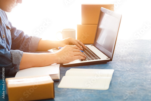 Young Asian men is accepting new orders from customers through laptops, business owner working at home office packaging on background, online shopping e-commerce or freelance working concept. photo