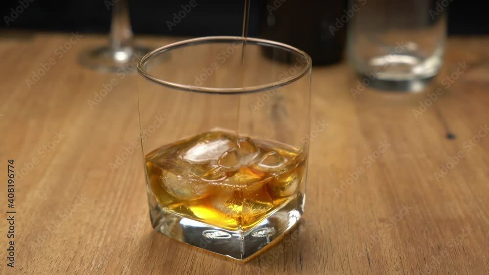 Pouring whiskey into glass filled with ice cubes on wooden table. Pouring whiskey into glass filled with ice cubes on wooden table.