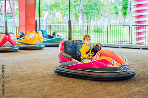 Boy wearing a medical mask during COVID-19 coronavirus having a ride in the bumper car at the amusement park