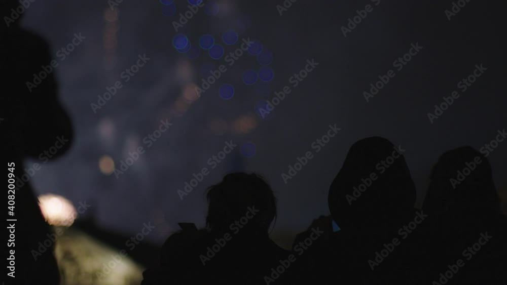 Fireworks in background with a silhouette of young family with mobile cell phone filming the fireworks display. Fireworks in background with a silhouette of young family with mobile cell phone filming the fireworks display.