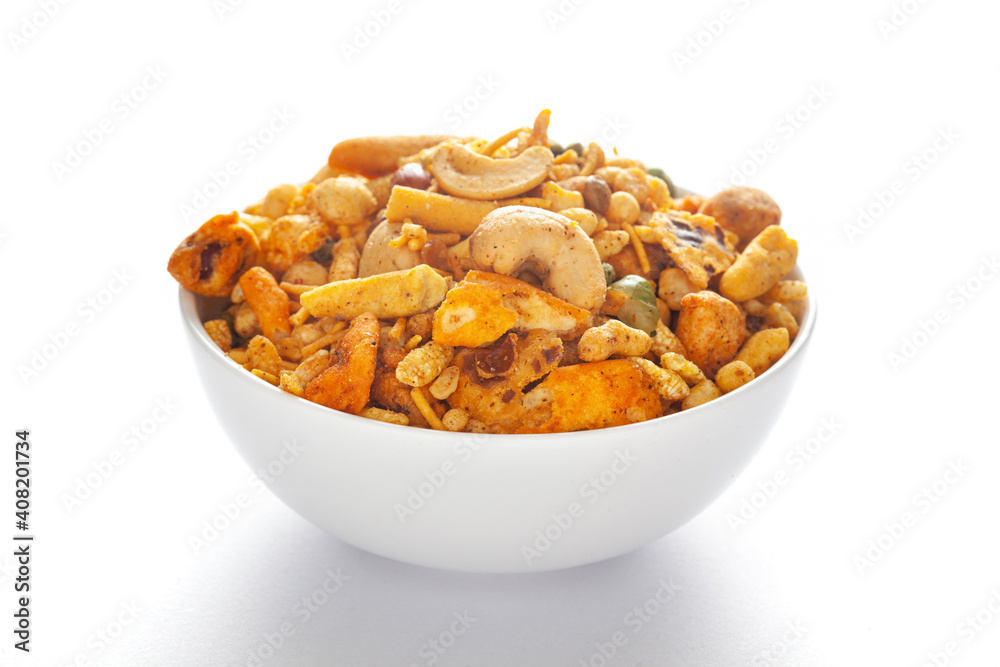 Fototapeta premium Pile of Indian spicy snacks (Namkeen) - 'All in one' in a white bowl, made with fried peanut, corn flakes, sweet pea, pulses, cashew nuts, etc. side view, against the white background.