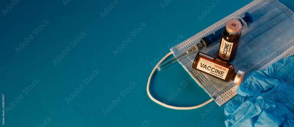 Coronavirus vaccine in bottles on blue background with copy space. Vials of medicine for covid19, syringe, medical face mask and gloves, top view. Immunization concept banner.