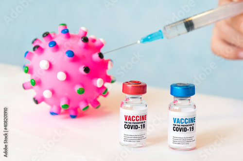 Two bottles of covid 19 coronavirus vaccine, toy virus and a syringe on white table. The medical conception of combating the covid-19 pandemic. photo