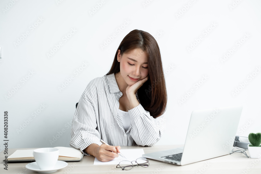 Asian female college students study online at home, enjoy extra lessons, watch videos, and take notes from a digital laptop, do homework by looking at the screen while sitting at a desk at home Asian female college students study online at home, enjoy extra lessons, watch videos, and take notes from a digital laptop, do homework by looking at the screen while sitting at a desk at home