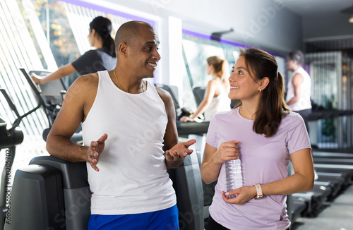 Sporty woman and man relaxing and talking on break during fitness workout at gym