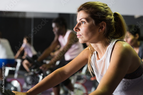 Portrait of sporty young adult woman doing cardio workout cycling bikes at fitness center