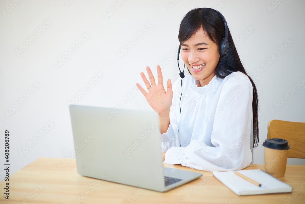 Asian woman wearing headphones and using laptop while via video conference.