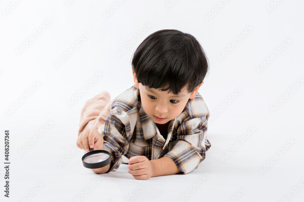 Child holding magnifying glass on white background. Boy with a magnifying glass in studio. Positive curious boy in casual wear looking at through magnifier Child holding magnifying glass on white background. Boy with a magnifying glass in studio. Positive curious boy in casual wear looking at through magnifier