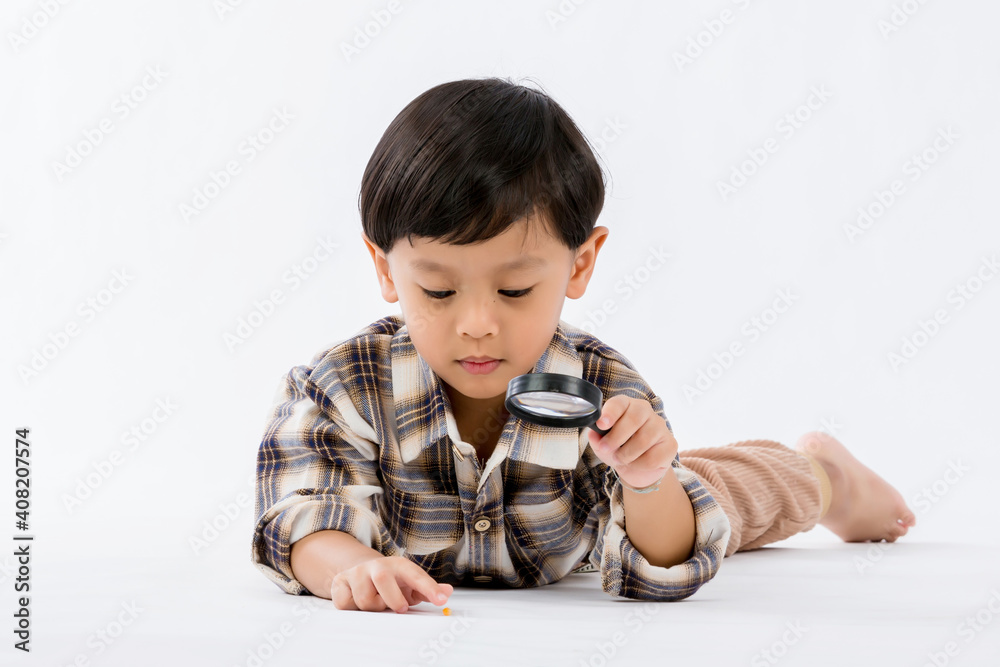 Child holding magnifying glass on white background. Boy with a magnifying glass in studio. Positive curious boy in casual wear looking at through magnifier Child holding magnifying glass on white background. Boy with a magnifying glass in studio. Positive curious boy in casual wear looking at through magnifier
