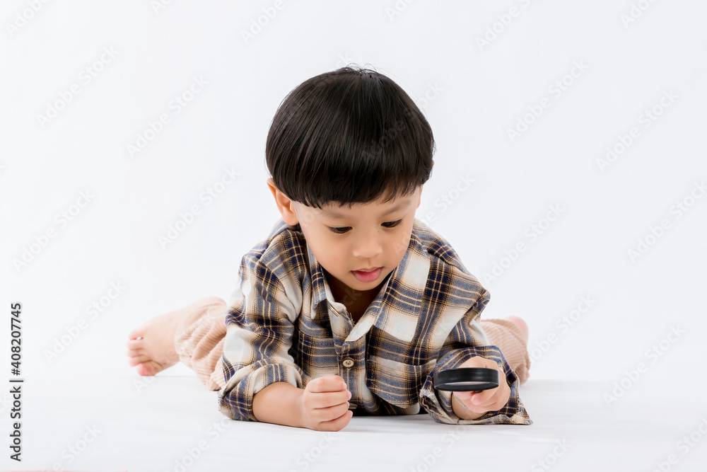 Child holding magnifying glass on white background. Boy with a magnifying glass in studio. Positive curious boy in casual wear looking at through magnifier Child holding magnifying glass on white background. Boy with a magnifying glass in studio. Positive curious boy in casual wear looking at through magnifier