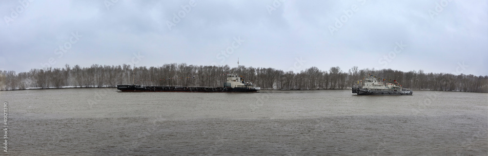 barge and pleasure boats sail along river in early spring against background of forest. Panoramic view.
