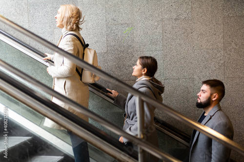Side view of focused people coming out of underground walkway, moving up on escalator..