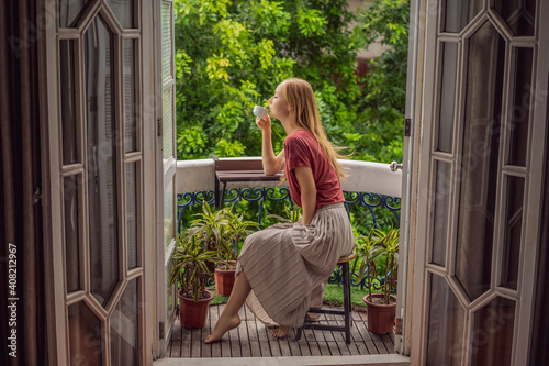 A ginger-haired woman stands on a heritage-style balcony enjoying her morning coffee. A woman in a hotel in Europe or Asia as tourism recovers from a pandemic. Tourism has recovered thanks to