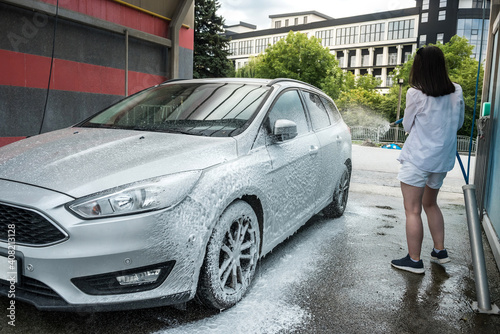 Ukrainian woman  with foam water gun cleans her car in service