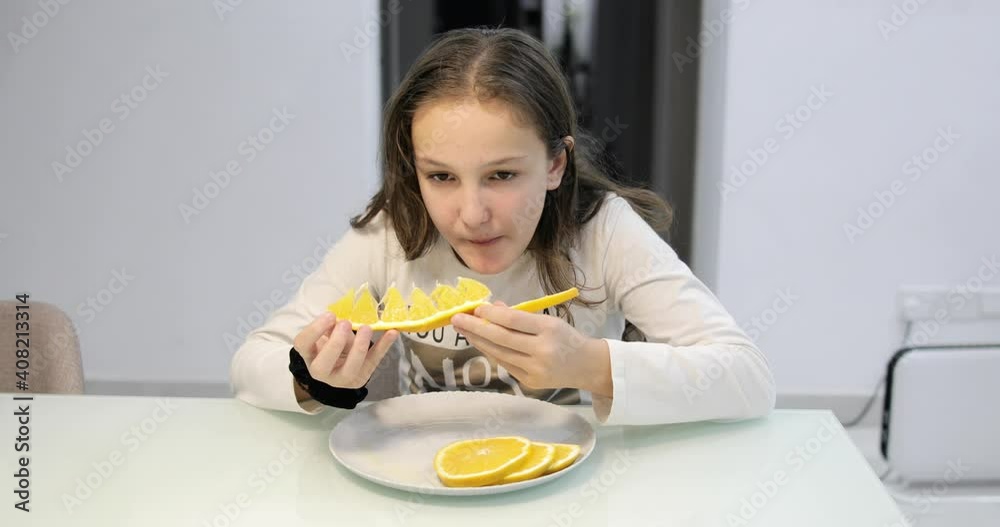 A girl eating juicy orange slices in the dining room. Steady camera shot.