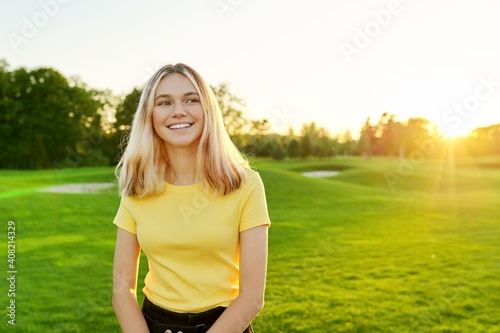 Outdoor portrait of smiling teenage girl 16, 17 years old in yellow T-shirt, on green sunny lawn photo