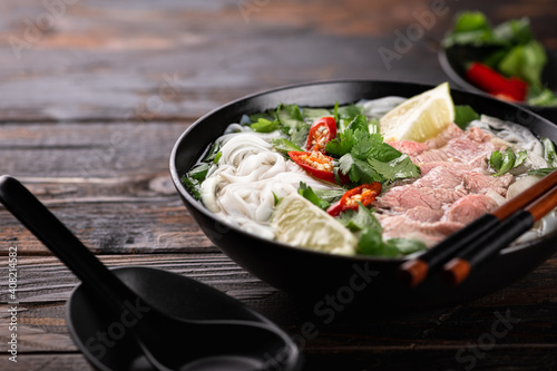 Vietnamese soup Pho Bo with beef and noodles on a wooden background, selective focus