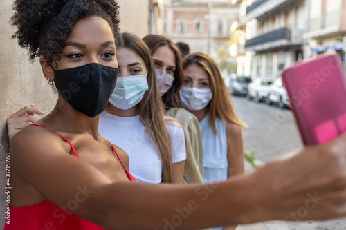 Happy multiracial friends taking a selfie and wearing protective face masks, concept of health care and the new normality photo
