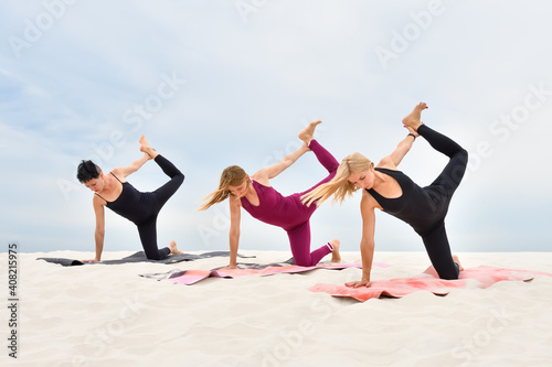 Three attractive young women perform yoga exercises on the beach