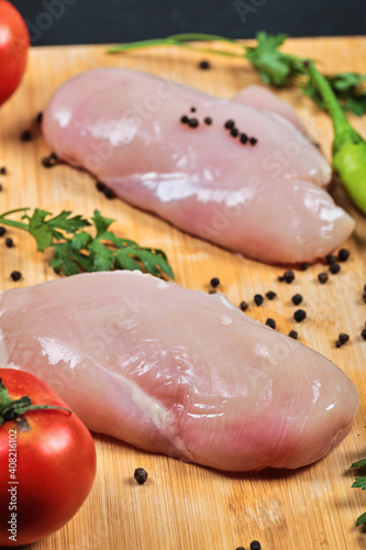 Raw chicken fillets on wooden board with fresh vegetables