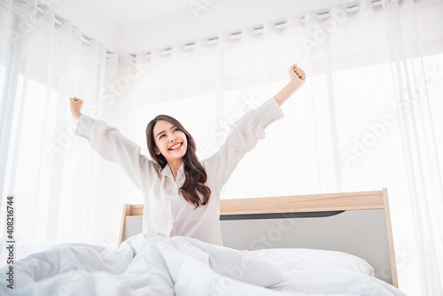 Fotografie Happy asian woman stretching hands in bed after wake up in the morning, Concept of a new day and joyful weekend